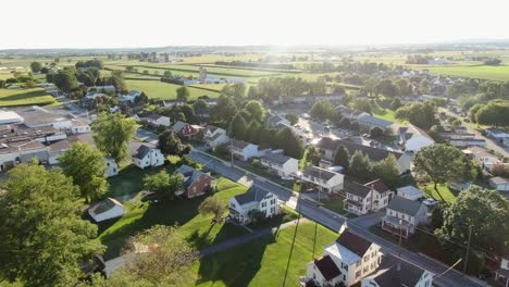 aerial pullback reveals small rural town community development, nearby farmland in pennsylvania, usa, united states neighborhood during summer magic hour