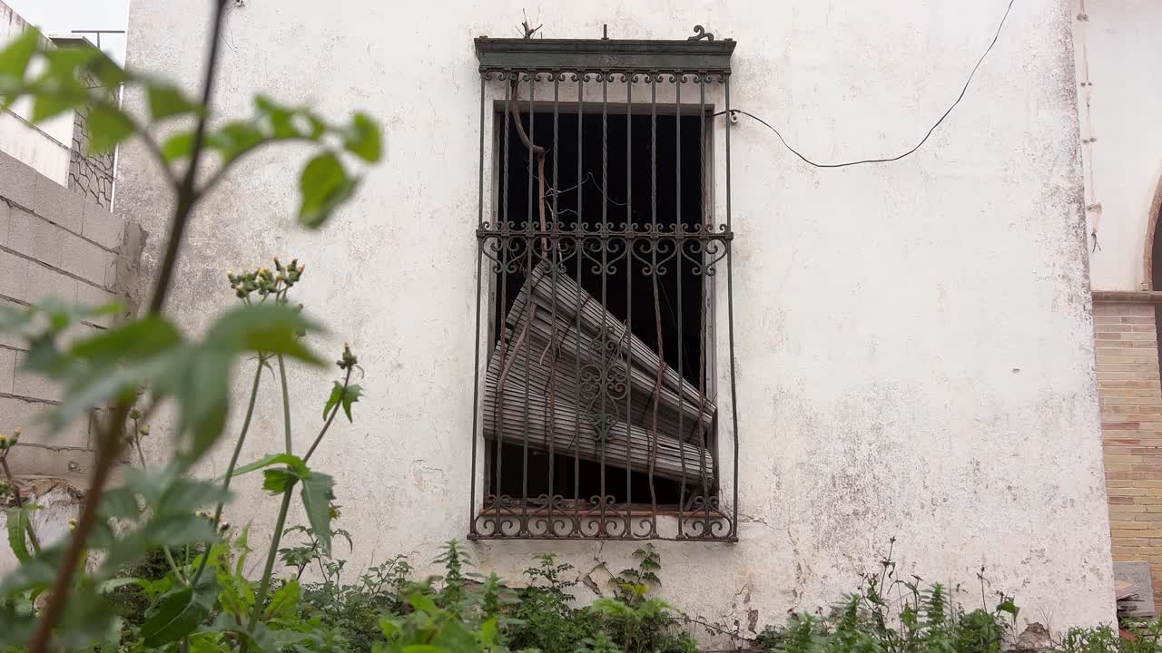 A window of an abandoned house with broken blinds and bars