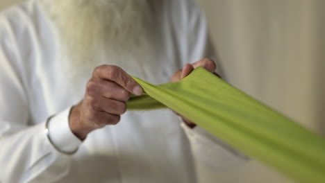 close-up-studio-aufnahme eines älteren sikh-mannes mit bart, der stoff für einen turban gegen einen einfachen hintergrund in echtzeit faltet 1