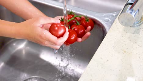 hands washing tomatoes under running water in a kitchen sink, emphasizing cleanliness and freshness