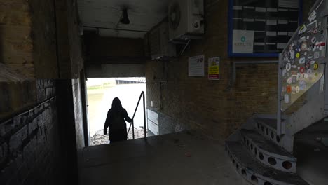 woman walks down old stone stairs toward the thames river in a moody, urban passageway