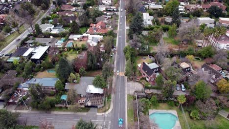 dolly in aerial view of a main street with little traffic and exclusive houses on the sides