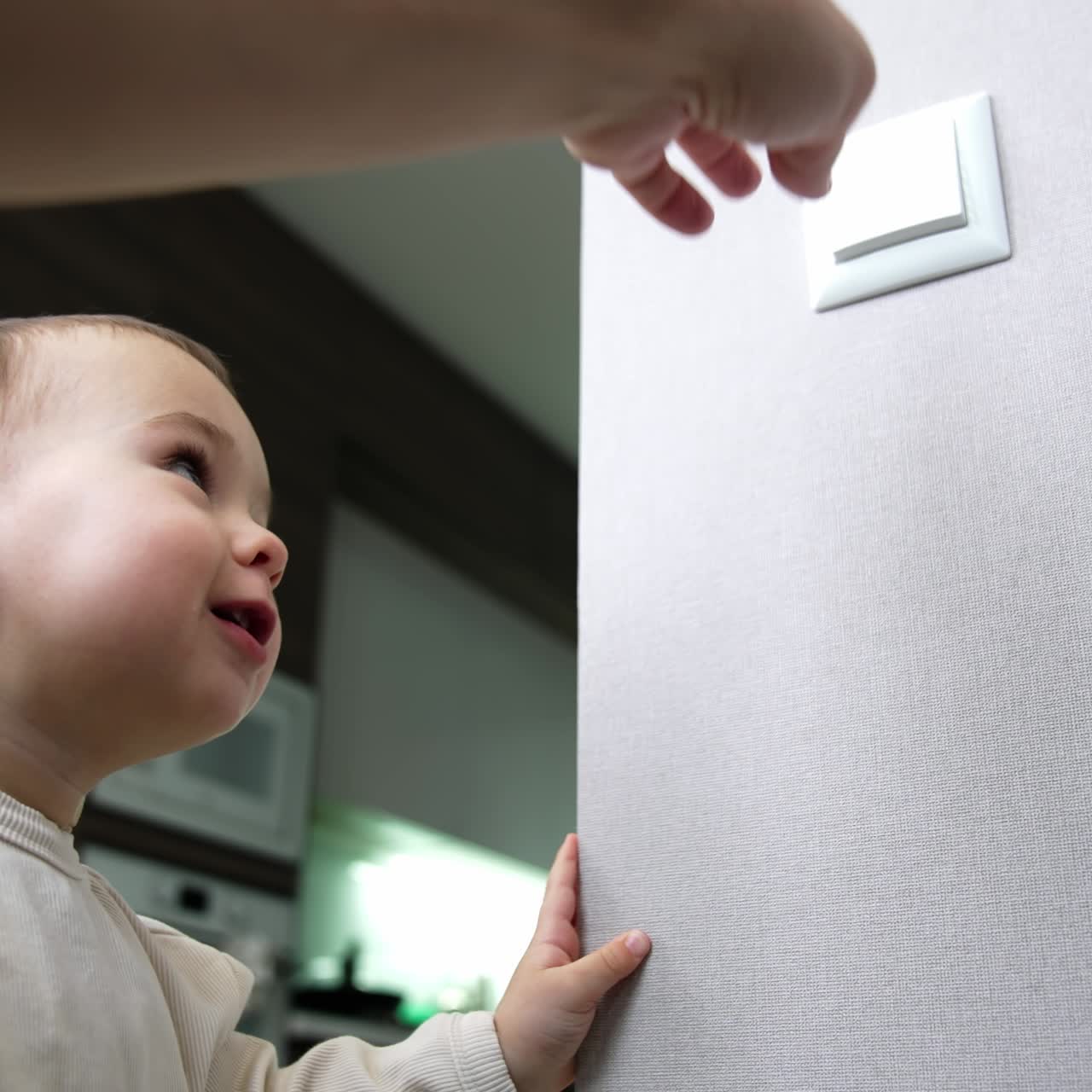 Happy toddler boy switches on the light in the room. Mom's hand switches off the light. Baby playing with illumination. Low angle view