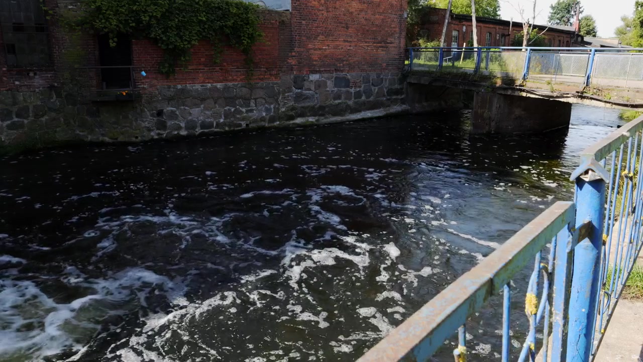 Vista panoramica di un canale urbano che scorre sotto un piccolo ponte con muri in pietra e ringhiere in metallo