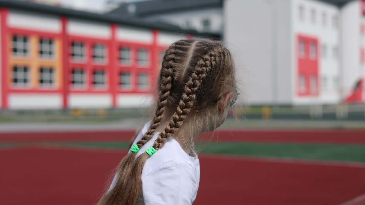 Una bambina con gli occhiali da sole corre e sorride nel parco. Una bambina elegante con una maglietta bianca. Una bambina con i capelli intrecciati