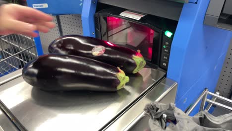 placing egg plants on self checkout scanner to weigh fruits and vegetables in big box superstore grocery market as the future of cashiers replacements