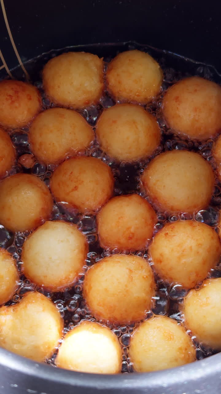 Round pot with lots of boiling oil and donuts frying in it. Close up view on the sweet yeast dough, Danish dough, preparation. Vertical video.