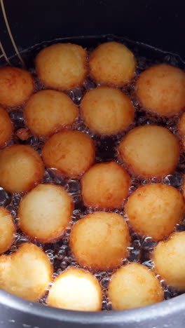 round pot with lots of boiling oil and donuts frying in it. close up view on the sweet yeast dough, danish dough, preparation. vertical video.