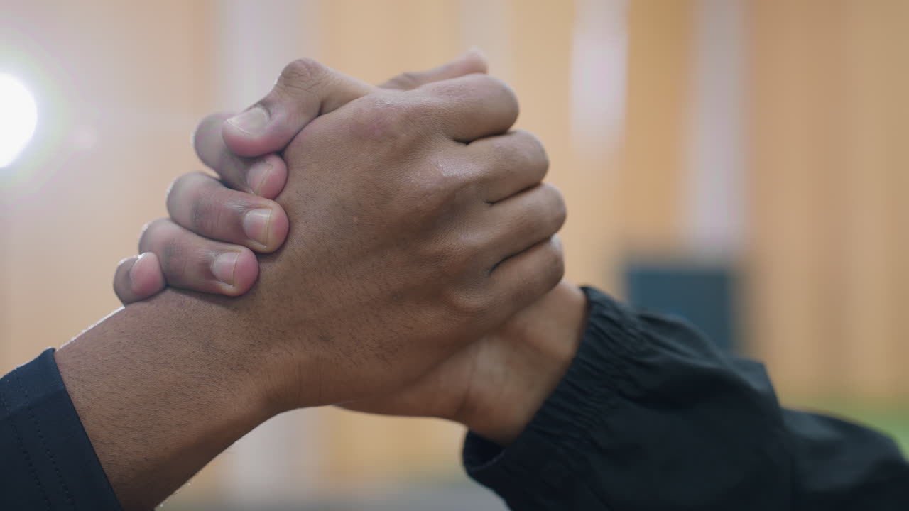 Close up of two men firmly shaking hands indoors with blurred background and bright light shining from behind symbolizing respect unity