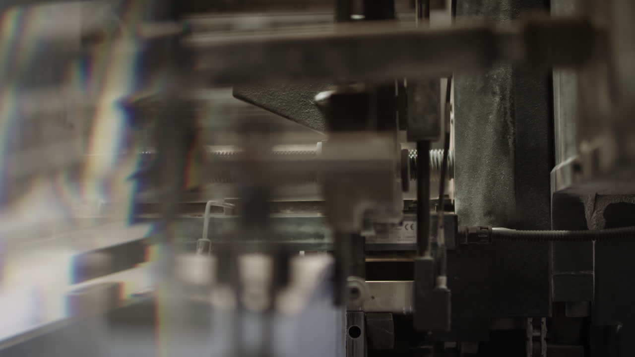 Inside of a printing machine, parts of machine moving, machine taking individual paper sheets from the pile and pushing it forwards on the production line