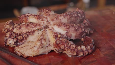 pulpo perfectamente cocinado colocado en una tabla de cortar de madera con vapores calientes que se vaporizan lentamente del delicioso pulpo tierno, toma de mano capturando detalles de los retoños en cada pierna