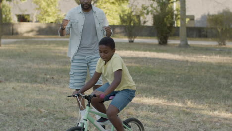 black boy learning riding bike while his father walking behind.