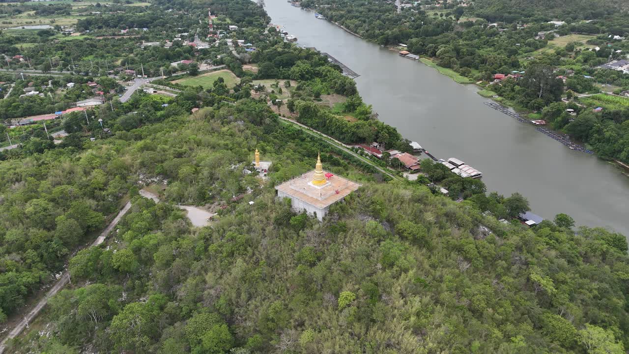 Stunning wide-angle aerial drone shot of a golden pagoda perched atop a lush hilltop in Saraburi Province, central Thailand