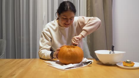 foto de una mujer joven tallando calabaza naranja en casa para halloween