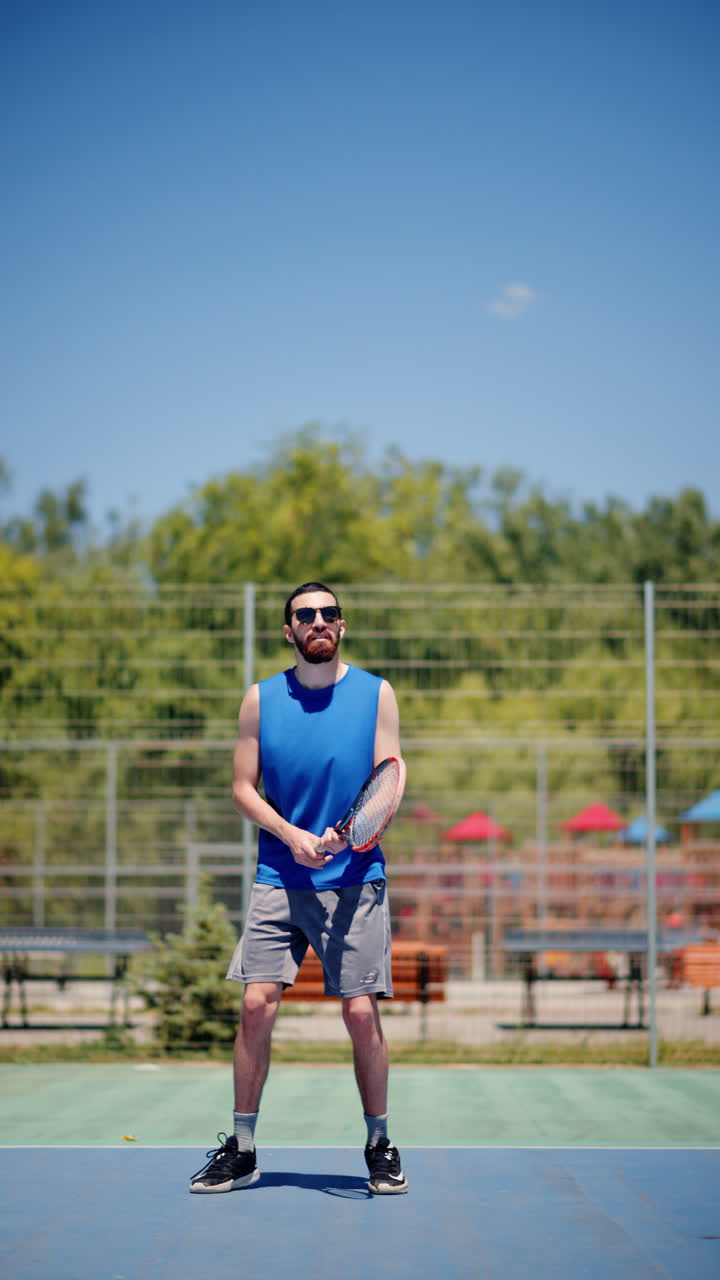 Man in blue shirt playing tennis on a blue and green court on a sunny day. Vertical
