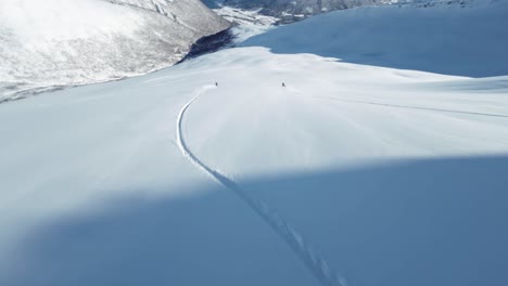 friends skiing down wild mountain slope, aerial fpv follow view