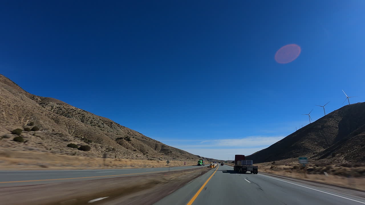 Driving through a narrow canyon on a highway with wind turbines on the hillside - point of view