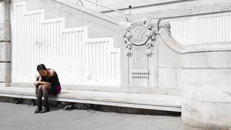 joven usando un teléfono inteligente en un banco en el stadtpark de viena, rodeada de arquitectura clásica, luz del día