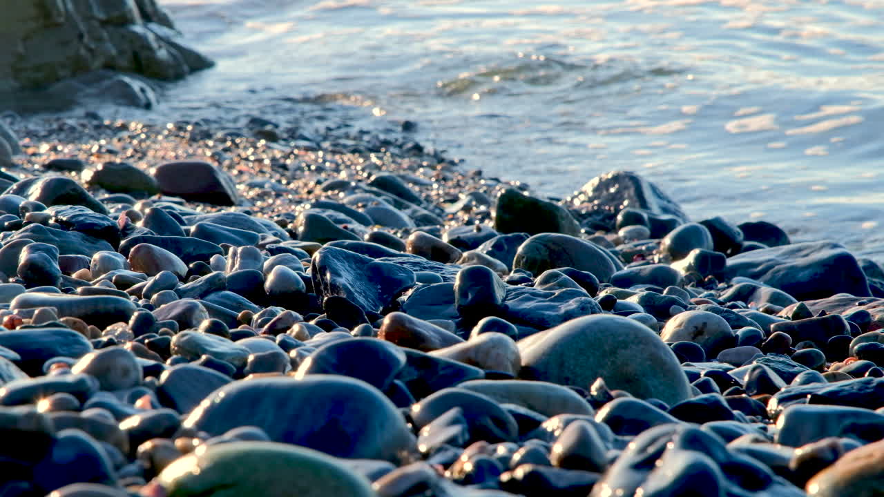Sunrise light glistens off wet smooth rocks as small ocean waves lap onto beach