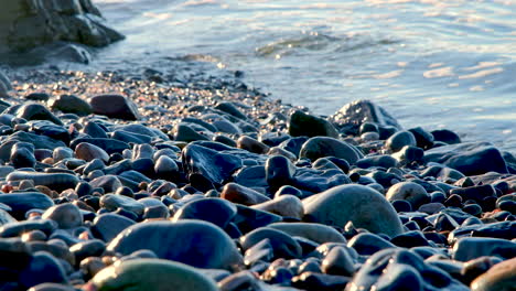 sunrise light glistens off wet smooth rocks as small ocean waves lap onto beach