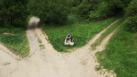 Zurückweichende-Drohnenaufnahme-Eines-Touristen,-Der-Auf-Einem-Felsen-In-Der-Mitte-Einer-Kreuzung-Im-Dorf-Tsarichina-Hole-In-Bulgarien-Sitzend-Zu-Sehen-Ist