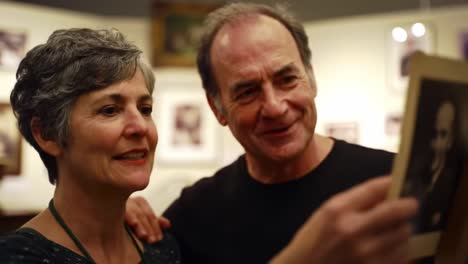 a heartfelt moment: couple reflecting on memories as they admire a vintage photograph in a cozy gallery setting, capturing their shared connection and emotion