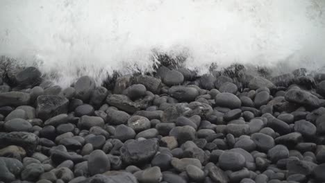 close up on pebbles as white winter waves crash in on beach at dunraven bay, south wales