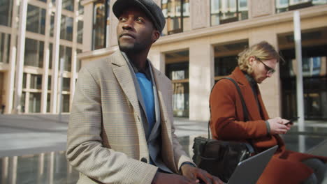 two multiethnic businessmen using laptop and smartphone outdoors