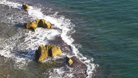 Rocky-coastline-with-waves-breaking-over-reef,-subtropical-mediterranean-sea-high-angle