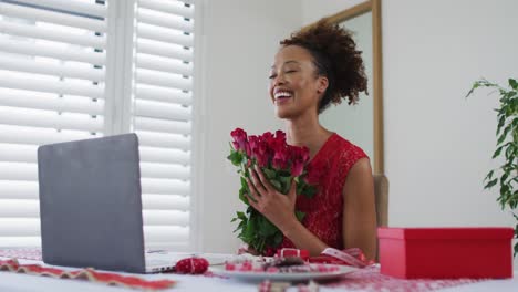 Feliz-Mujer-De-Raza-Mixta-En-Una-Videollamada-De-Una-Cita-De-San-Valentín,-Sosteniendo-Rosas-Rosadas