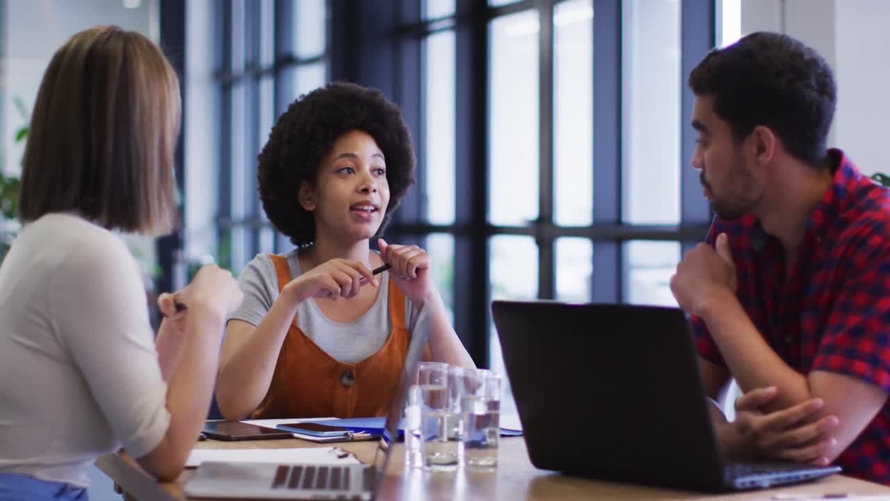 Diverse business people sitting using laptop going through paperwork in modern office