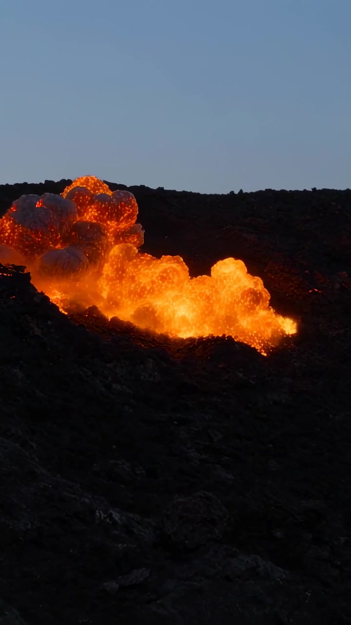 Video verticale: Luce intensa che emerge da una fessura della cresta, lava che si riversa lungo il pendio, sprigionando fumo.