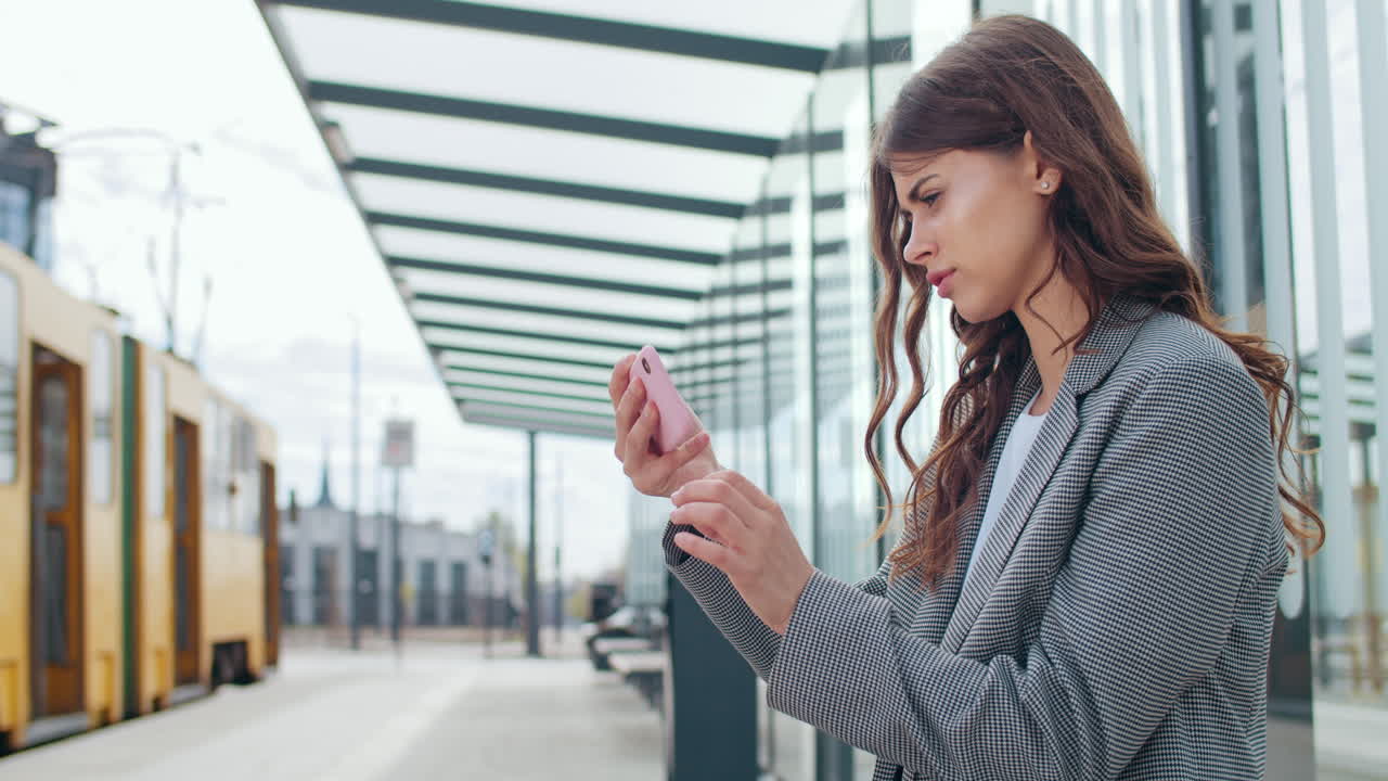Young Woman Using Smartphone While Waiting at a Modern Tram Station
