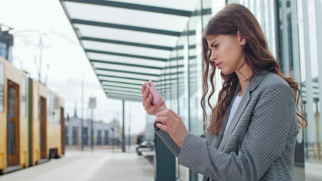 young woman using smartphone while waiting at a modern tram station