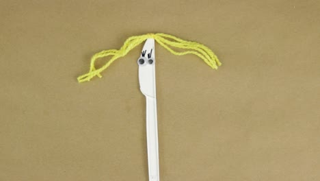 Gluing-yellow-yarn-hair-to-disposable-plastic-knife-with-googly-eyes