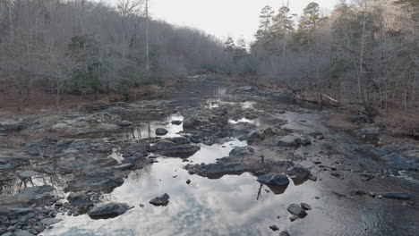 tranquil rocky river flowing through leafless forest in fall, aerial