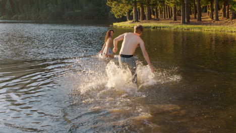 glückliches paar, das bei sonnenuntergang im see spritzt, junger mann holt seine freundin ab, spritzt im wasser, macht spaß, spielt, genießt romantische sommerliebe