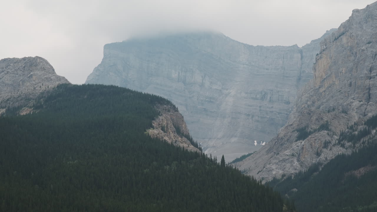 Dramatic Banff mountain vista, towering peaks shrouded in mist contrasting with forested slopes