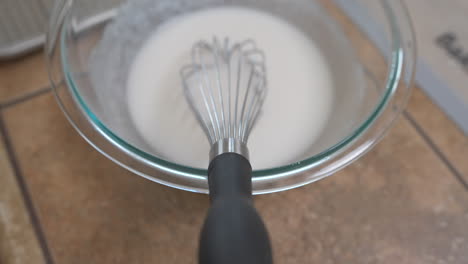 whisk in bowl of white icing glaze on countertop, overhead detail approach