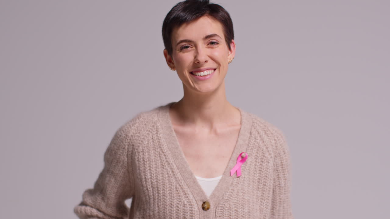 retrato de estudio de una joven sonriente que lleva una cinta rosa de concienciación sobre el cáncer de mama contra un fondo blanco 1