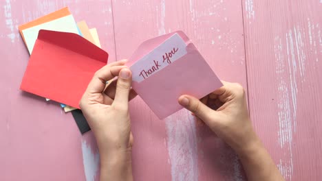 hands holding a thank you note in a pink envelope