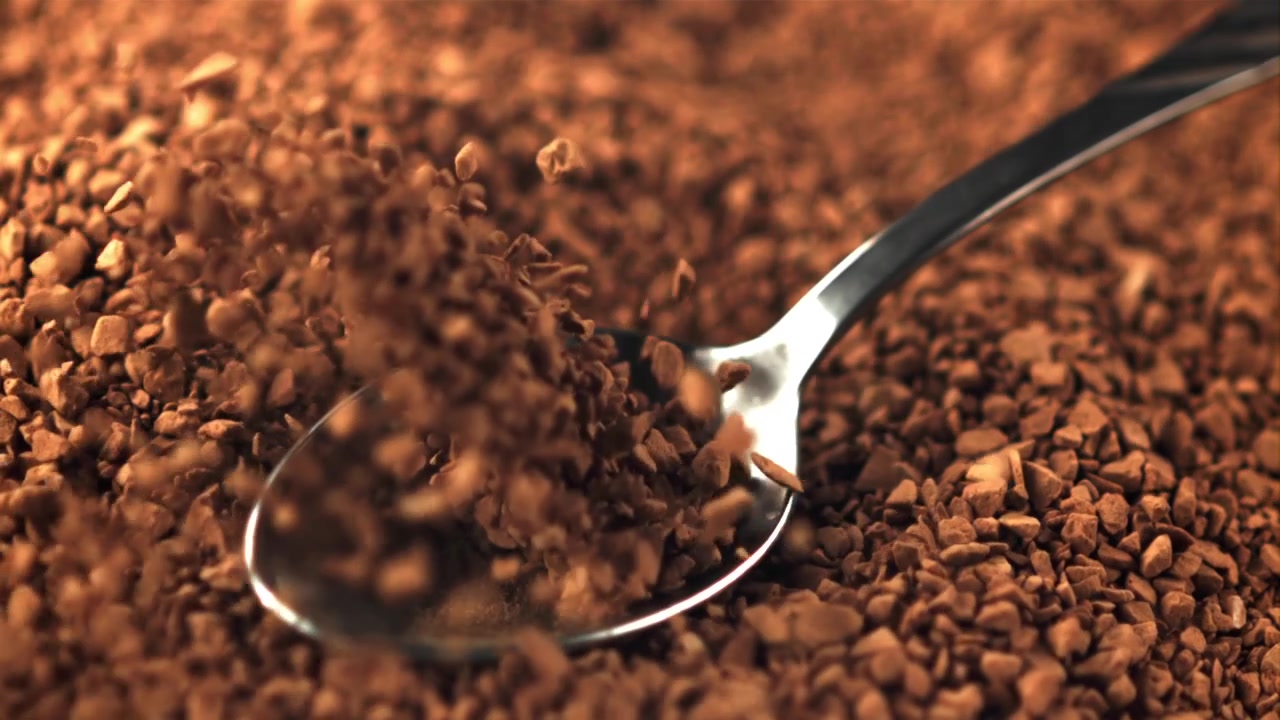 Granuli di caffè istantaneo che cadono su un cucchiaio al rallentatore.
