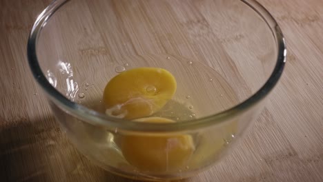 two fresh eggs cracked and poured into a glass bowl