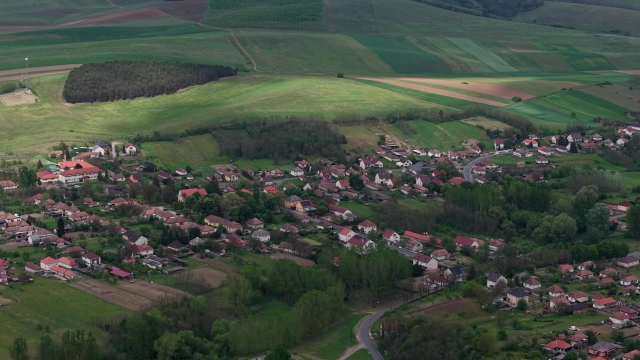 Letecký pohled dronem na malebnou vesnici obklopenou rozlehlými, zvlněnými zelenými poli a lesy v klidném údolí.