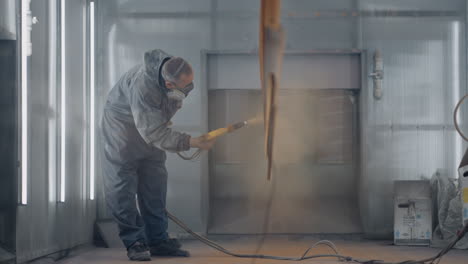 a man in a respirator is painting metal . production of steel and metal structures. painting shop. the painter works with a spray gun paint is applied