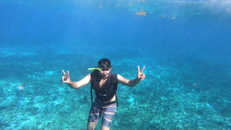 a boy freestyle diving in deep blue sea and cheering with peace sign enjoying diving experience | tourist diving in ocean with gears, mask, life jacket and fins on