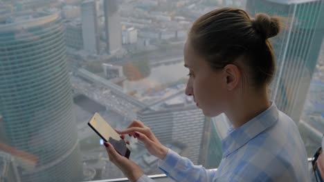 mujer usando un teléfono inteligente contra la vista del paisaje urbano a través de la ventana de un rascacielos