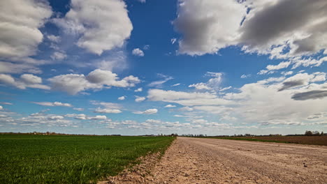 a dynamic cloudscape over a countryside dirt road and grassy field - zoom out time lapse