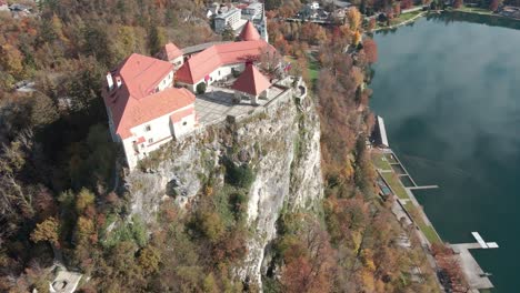 Toma-Aérea-De-Un-Castillo-Cerca-De-Un-Lago-Encaramado-En-Una-Roca-Alta-En-Las-Montañas-De-Eslovenia,-Lago-Sangrado