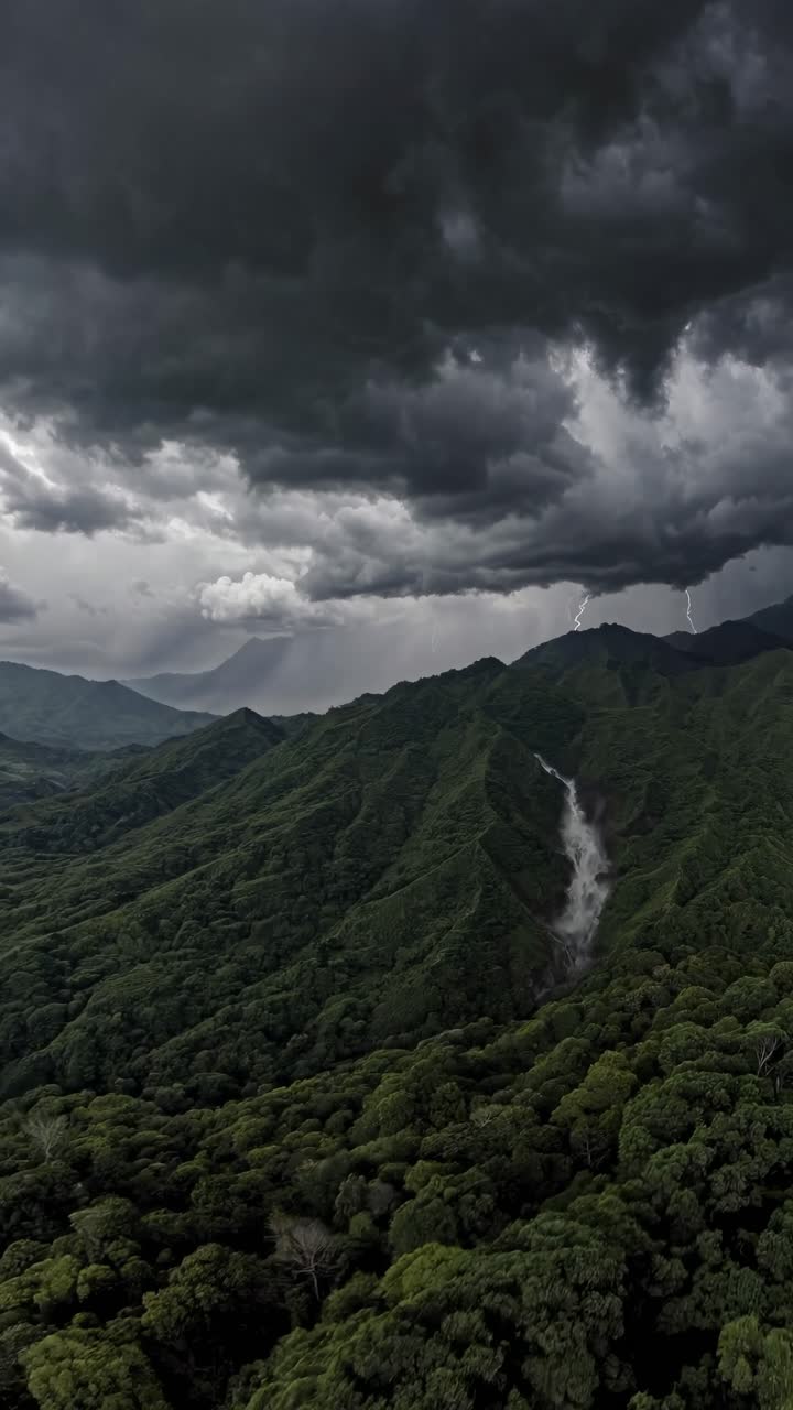 Aerial video captures dramatic storm clouds over lush green mountains, with a waterfall visible